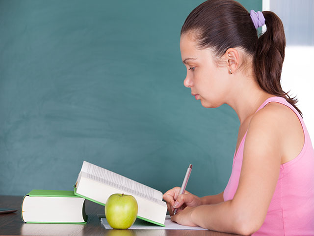 Portrait of young female student writing on paper beside green apple